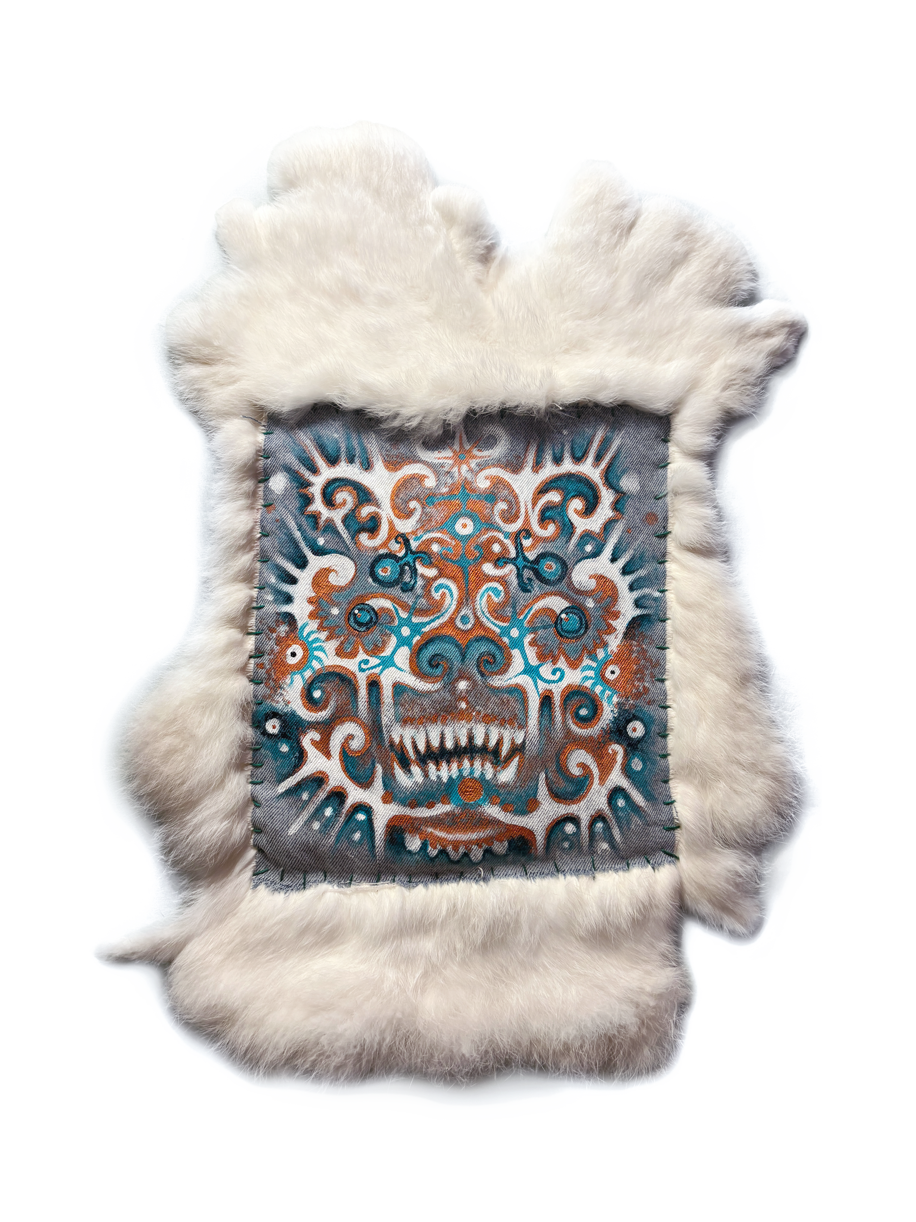 A square of painted fabric with an ornate teal, rust and white face baring its fangs, stitched into a border of bone-white fur.