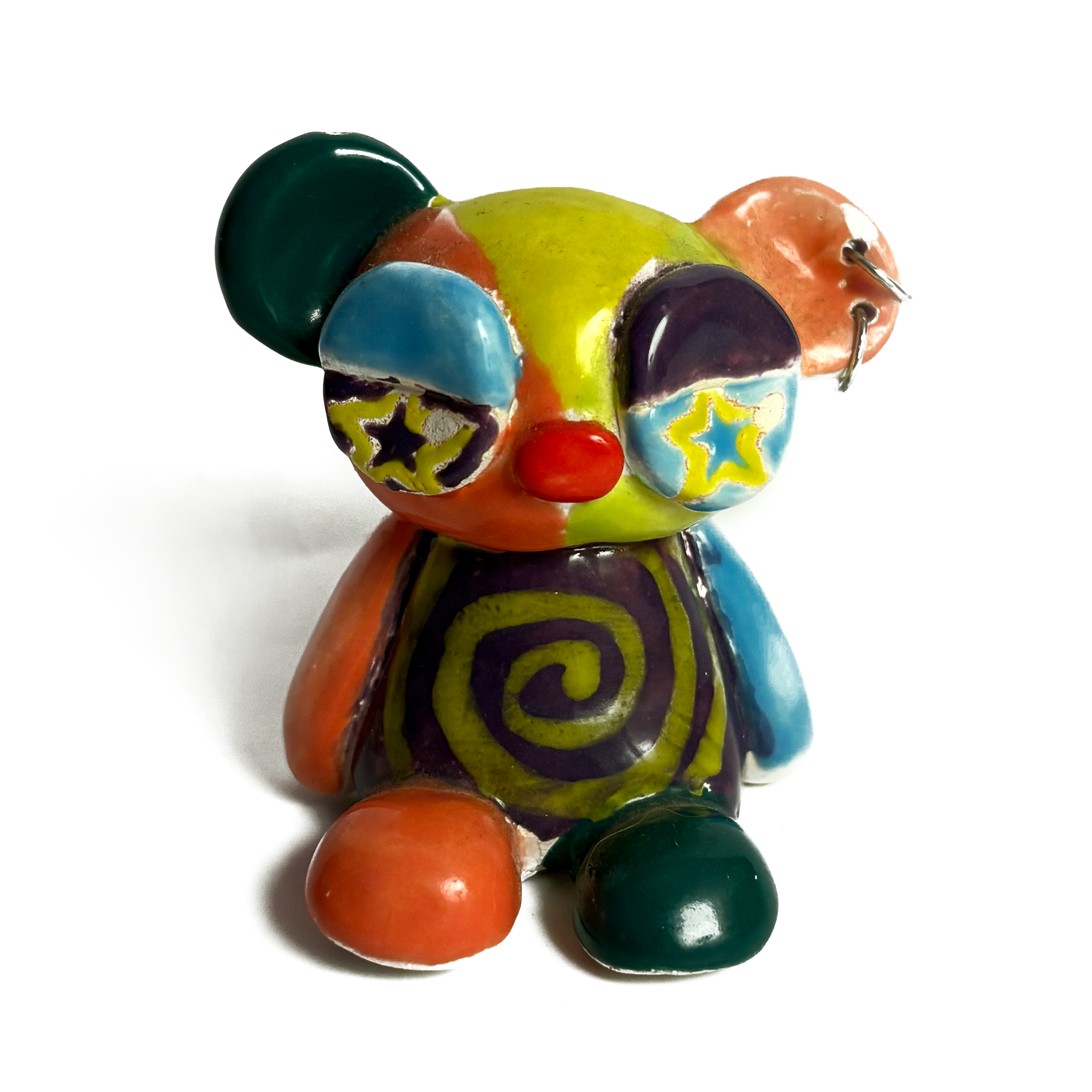 Ceramic bear in patchwork glazes of lime, orange, teal and purple, with star-shaped eyes, a red nose, a spiral on its belly and rings through one ear.