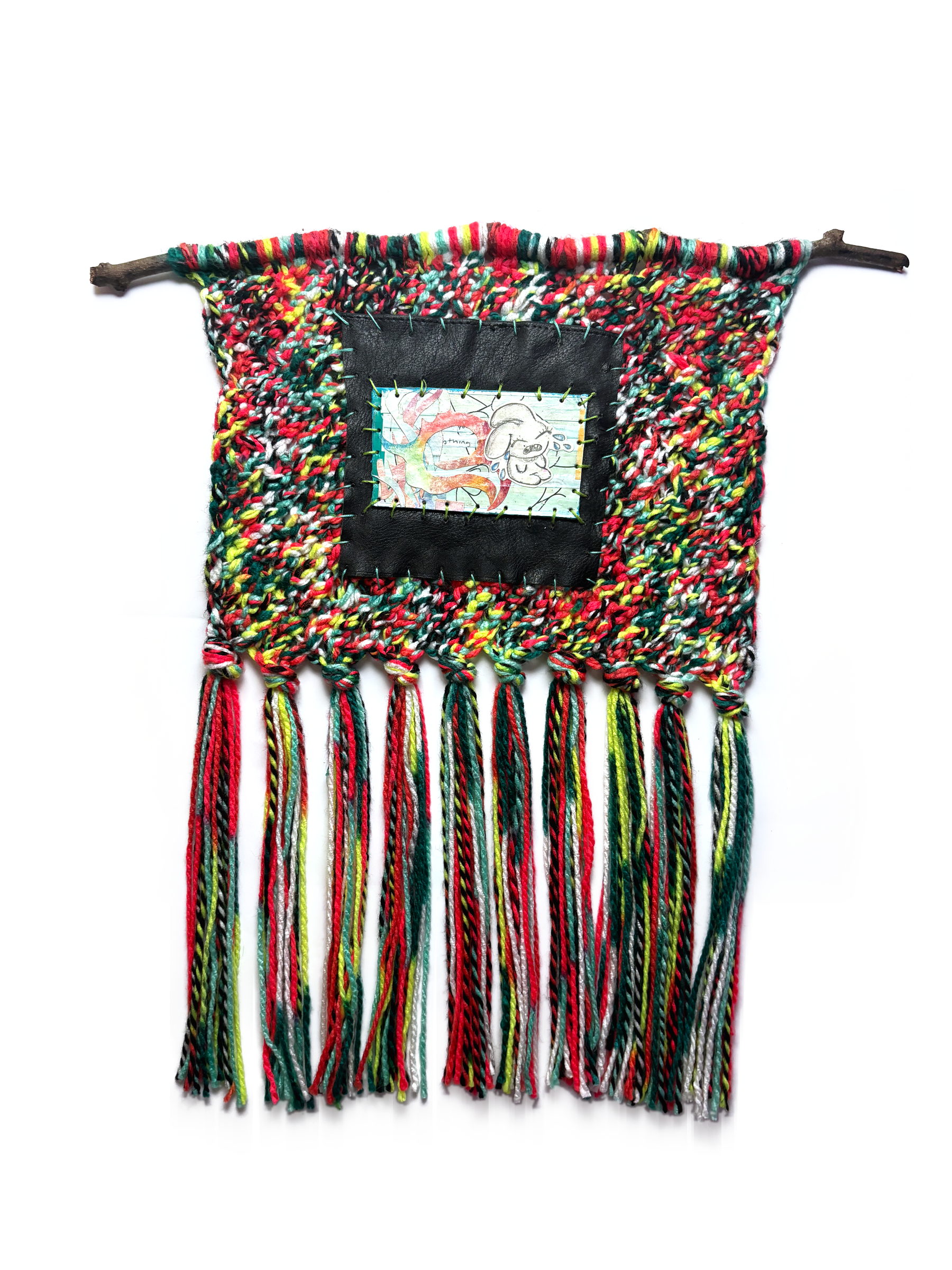 Wall hanging on a branch: chunky knitted yarn in red, green and white with a long fringe, and a black panel framing a small drawing.