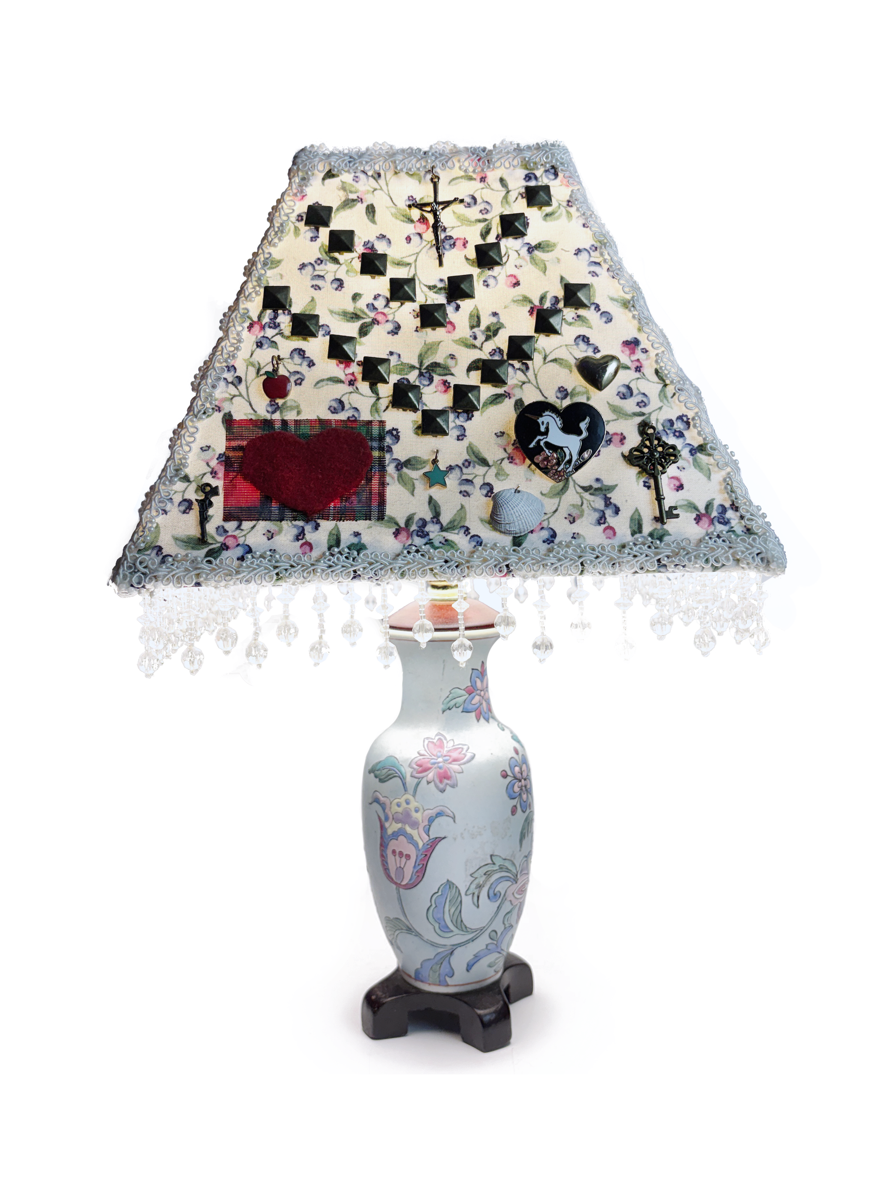 The same lamp turned: the shade's floral fabric is studded with black pyramid studs, a red heart patch, a small crucifix, charms and a heart-shaped horse pin.