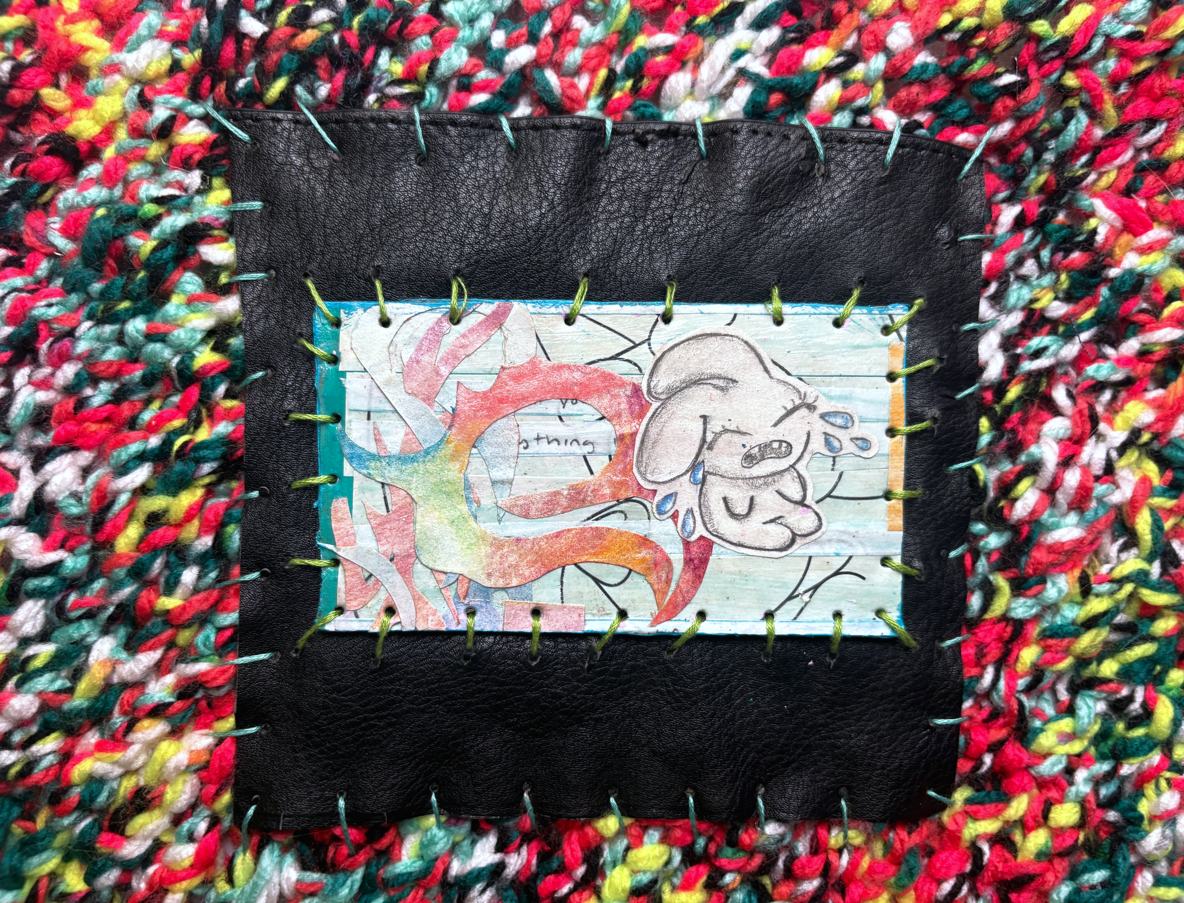 Close-up of the black panel, stitched with green thread, framing a pastel drawing of a weeping white creature and a red swirl.