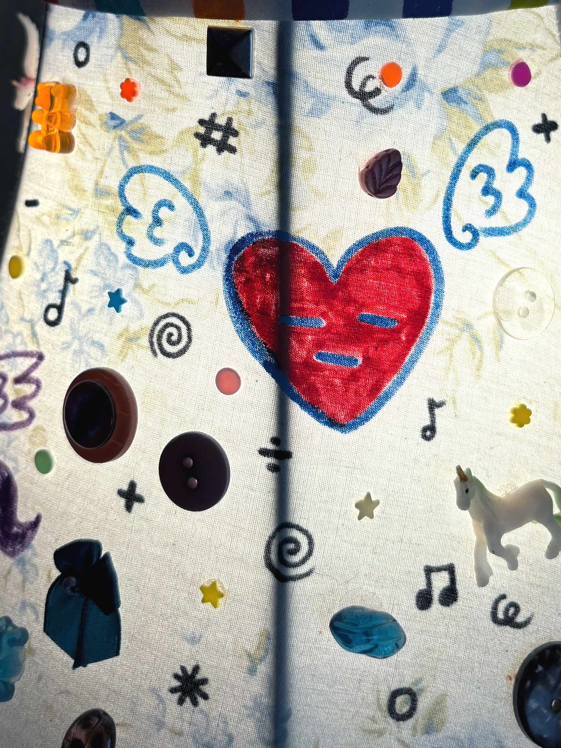 Close-up of the shade: a red stitched heart with a sleepy face, drawn blue wings, buttons and a small unicorn.